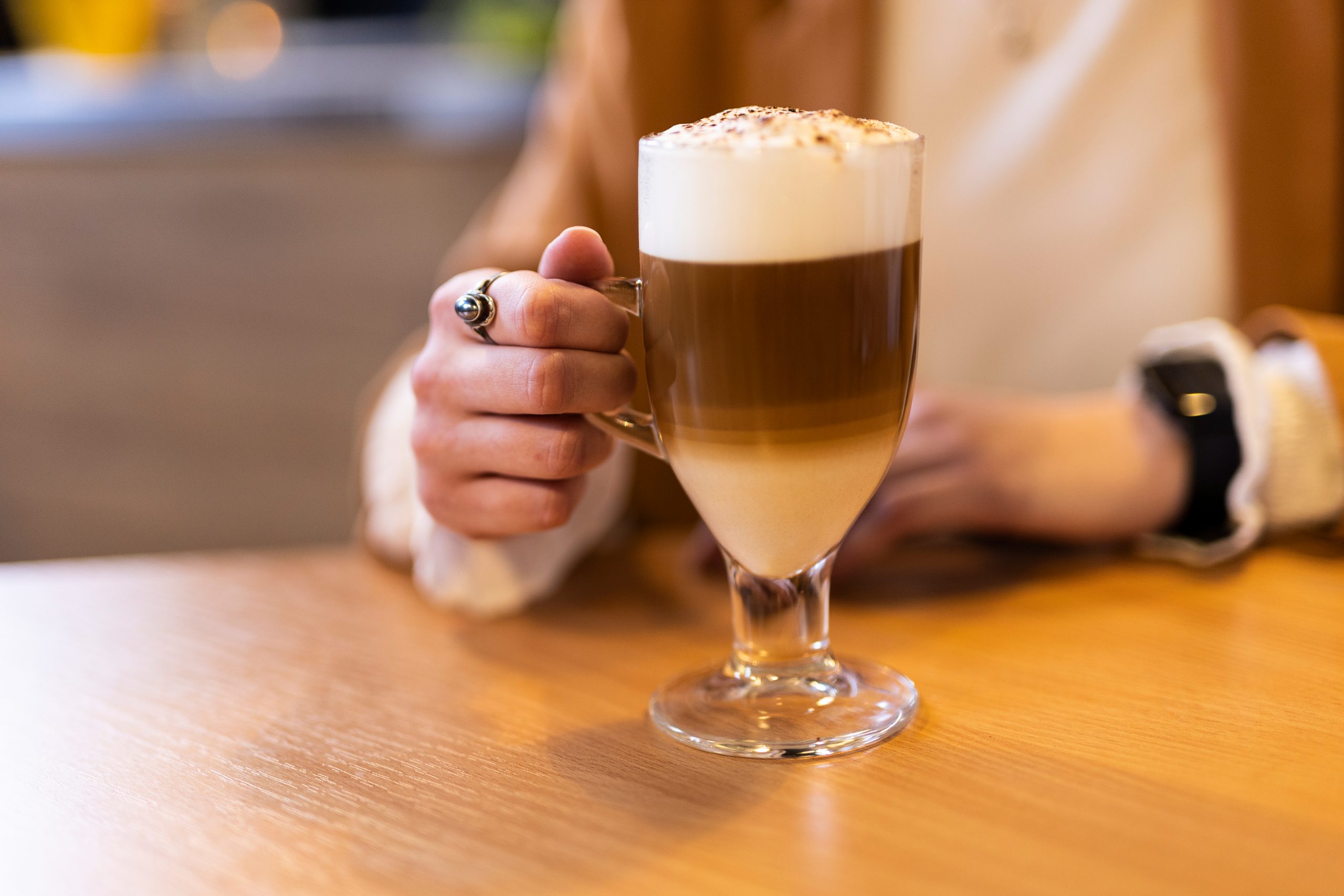 kawa latte z pianą i posypką w szklance, szklanka trzymana przez damską dłoń
