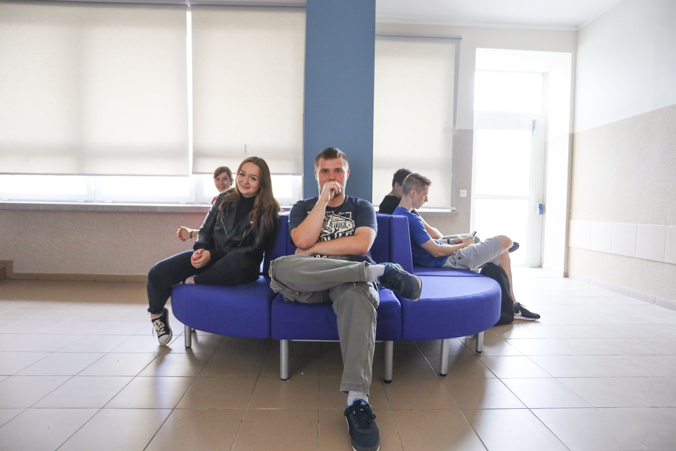 5 młodych osób siedzi na niebieskich sofach w szkole