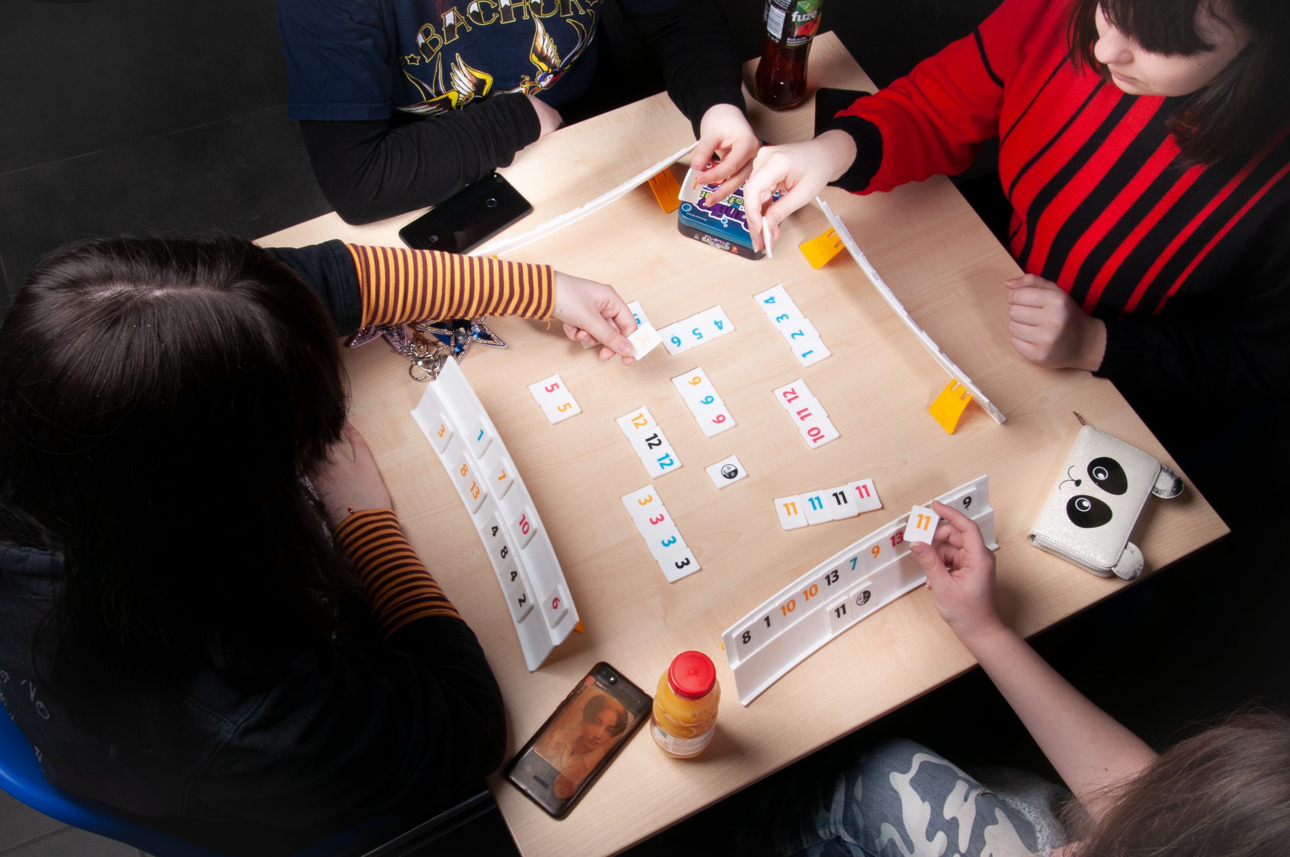 cztery młode osoby grają w grę planszową, na stoliku rozłożone elementy gry