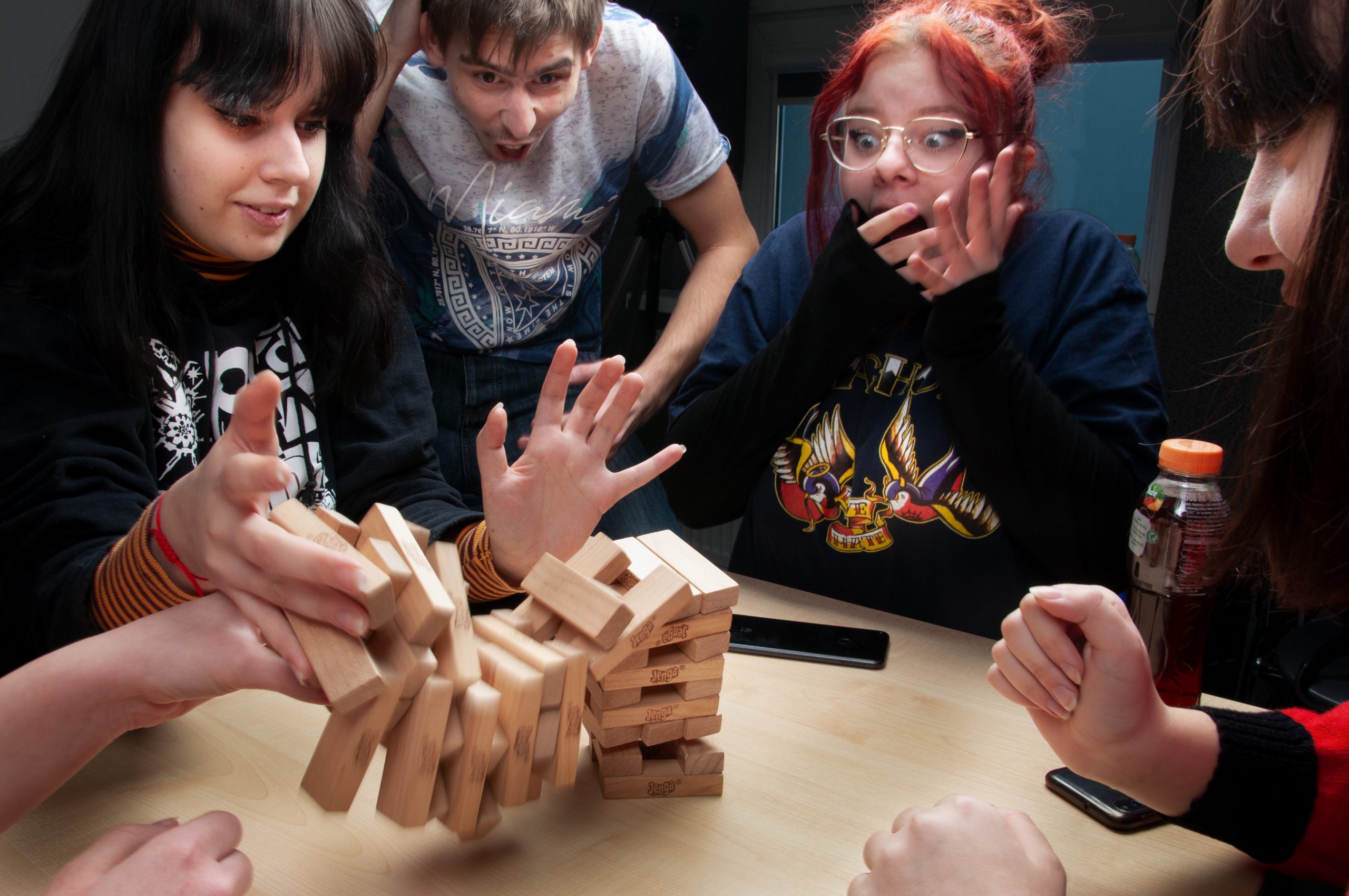 cztery młode osoby grają w grę Jenga, klosku rozsypują się na blat stolika