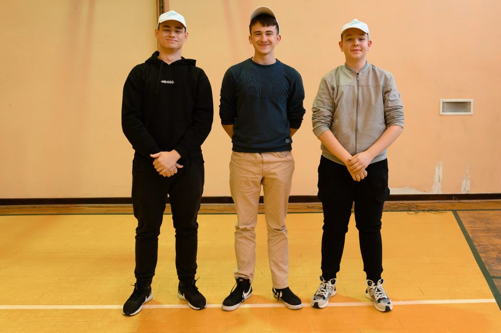 trzech uczniów stoi, na głowach białe czapki