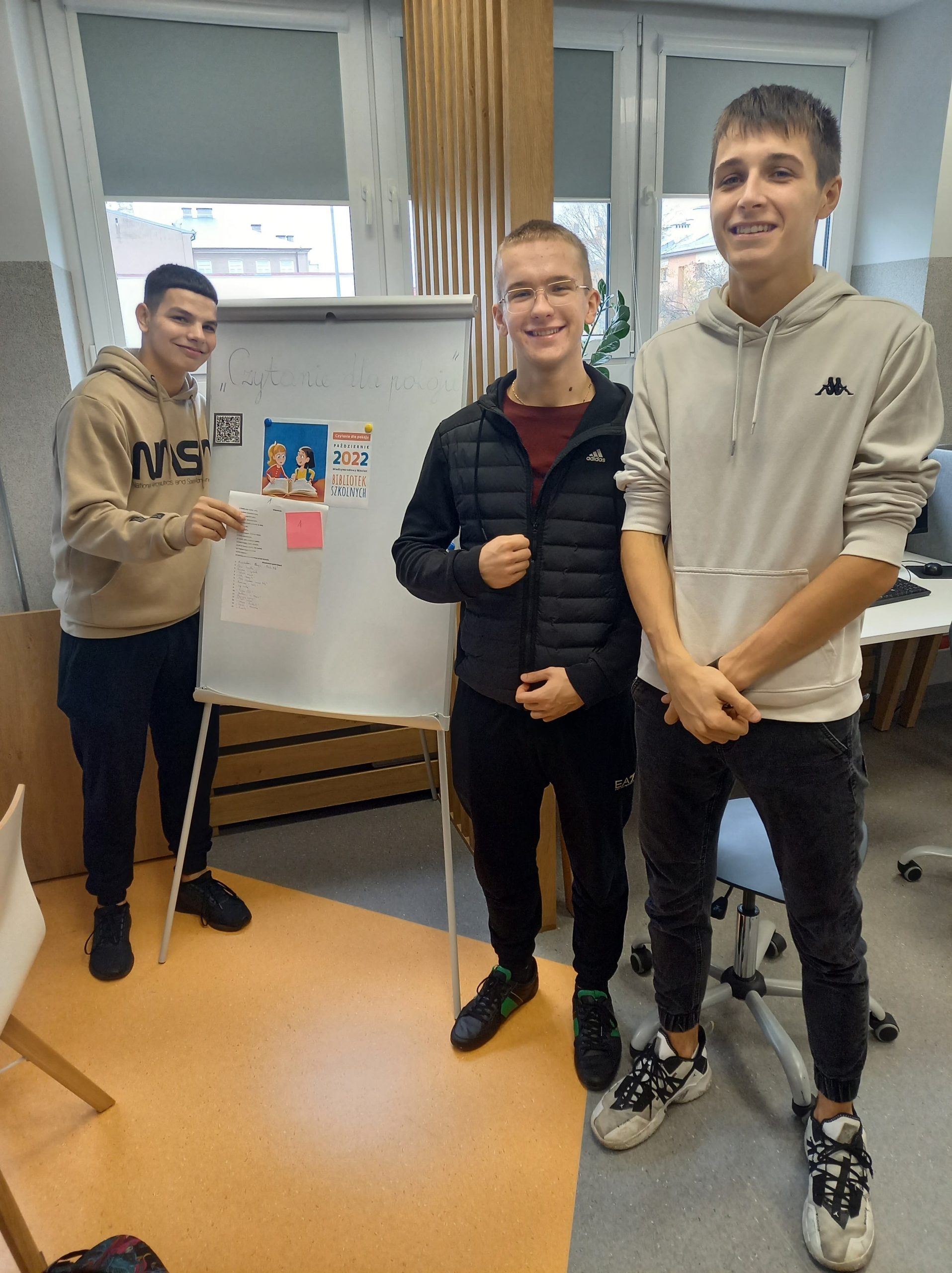 trzech młodych chłopców stoi na tle białej tablicy