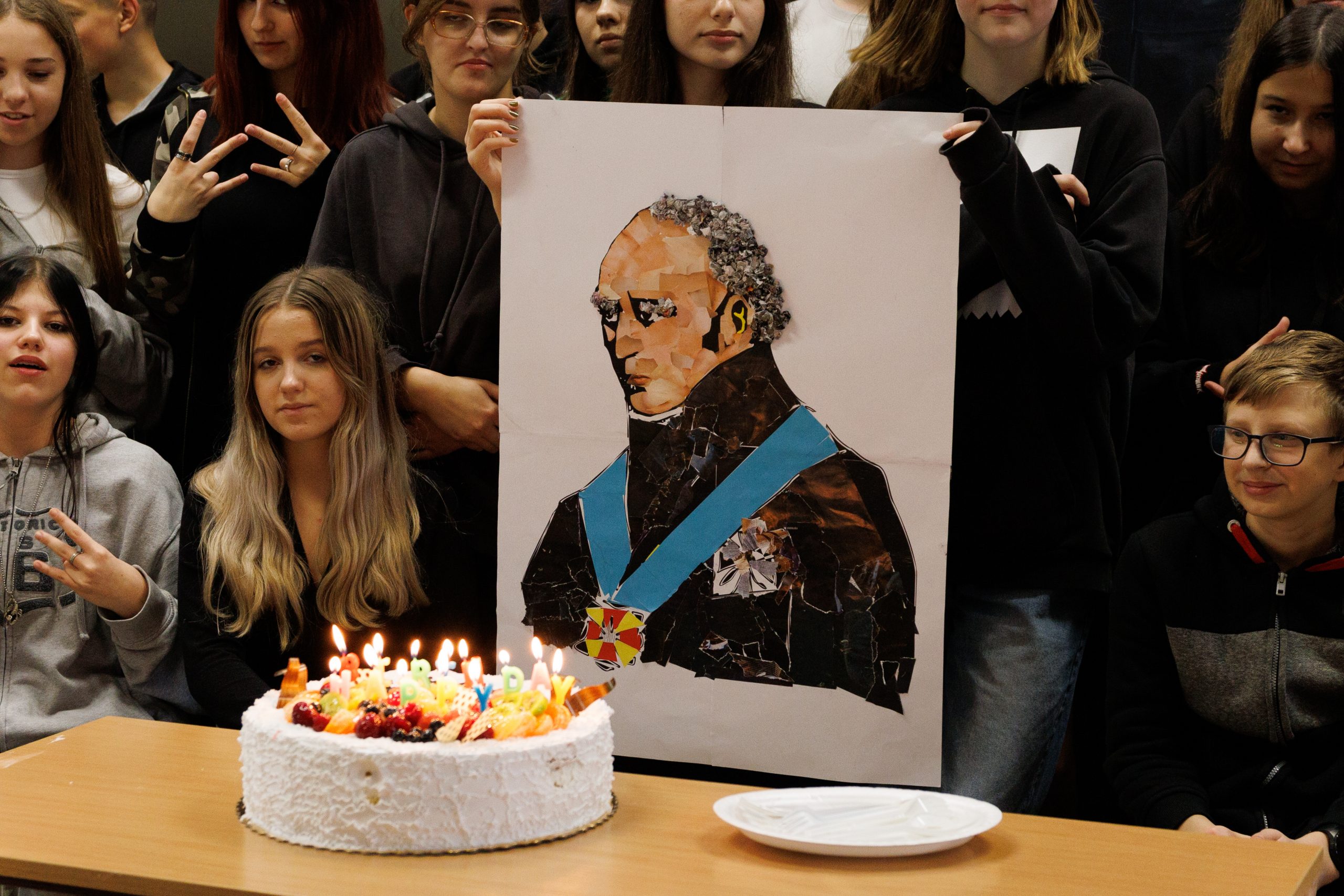 grupa ludzi pozuje do zdjęcia, na pierwszym planie tort ze świeczkami i portret Stanisława Staszica