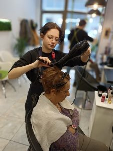 młoda dziewczyna w salonie fryzjerskim suszy włosy kobiecie