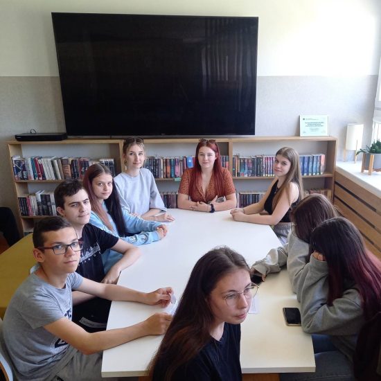 grupa uczniów siedzi przy stole w bibliotece szkolnej