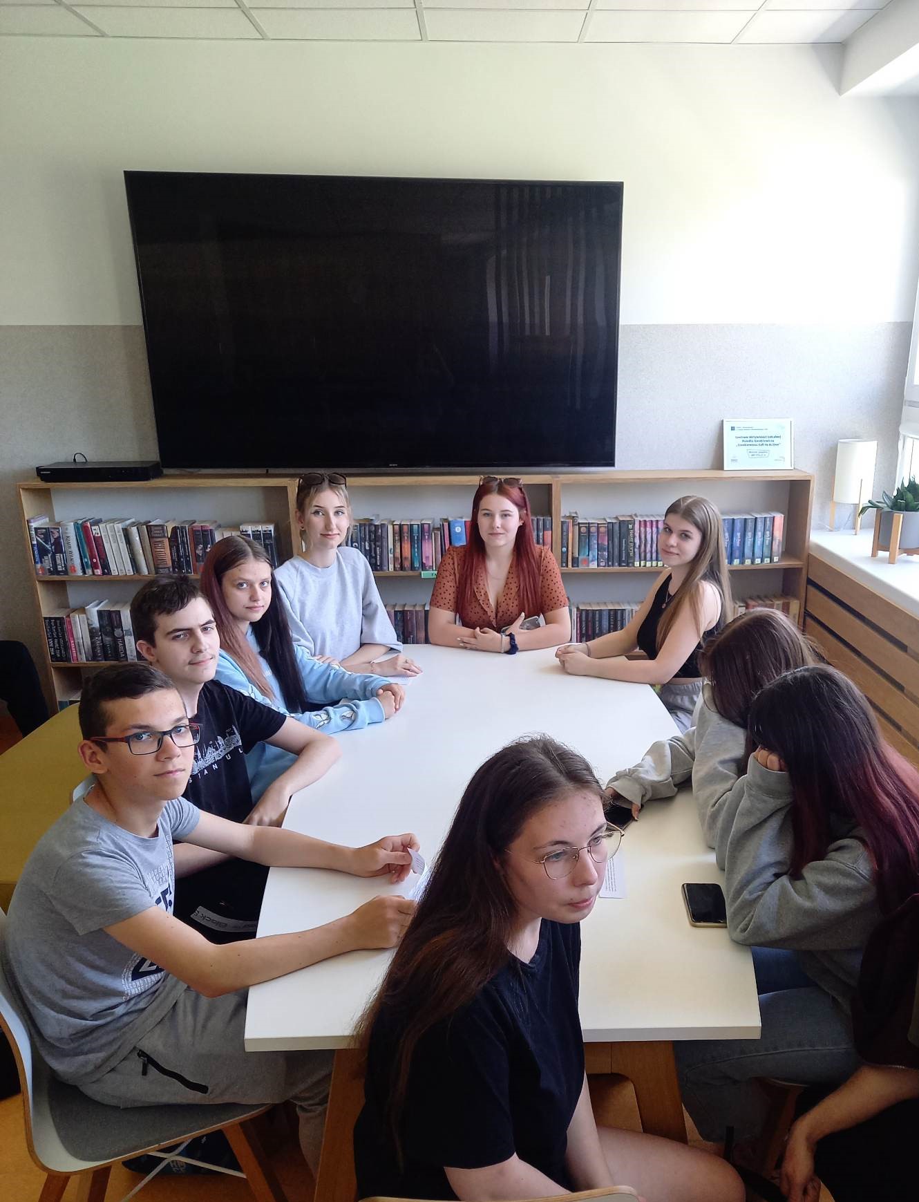 grupa uczniów siedzi przy stole w bibliotece szkolnej