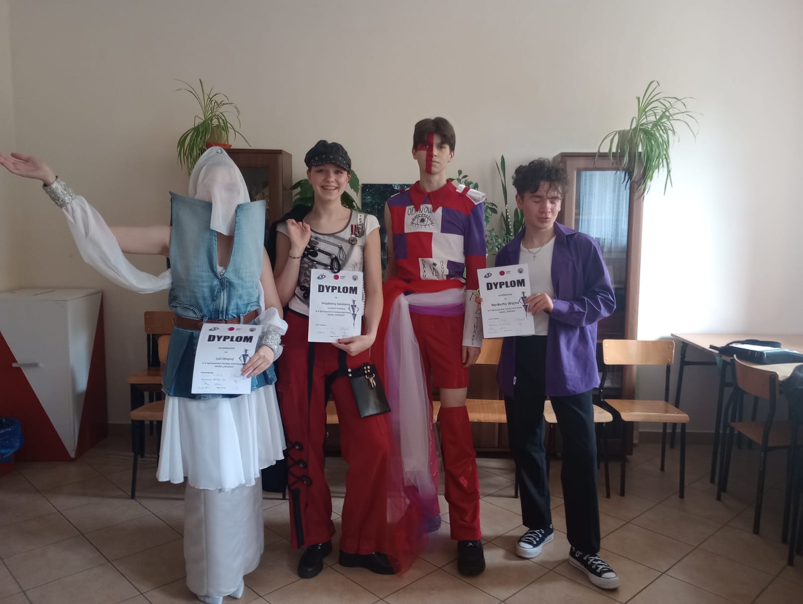 4 uczniów w modowych strojach, w rękch trzymają dyplomy