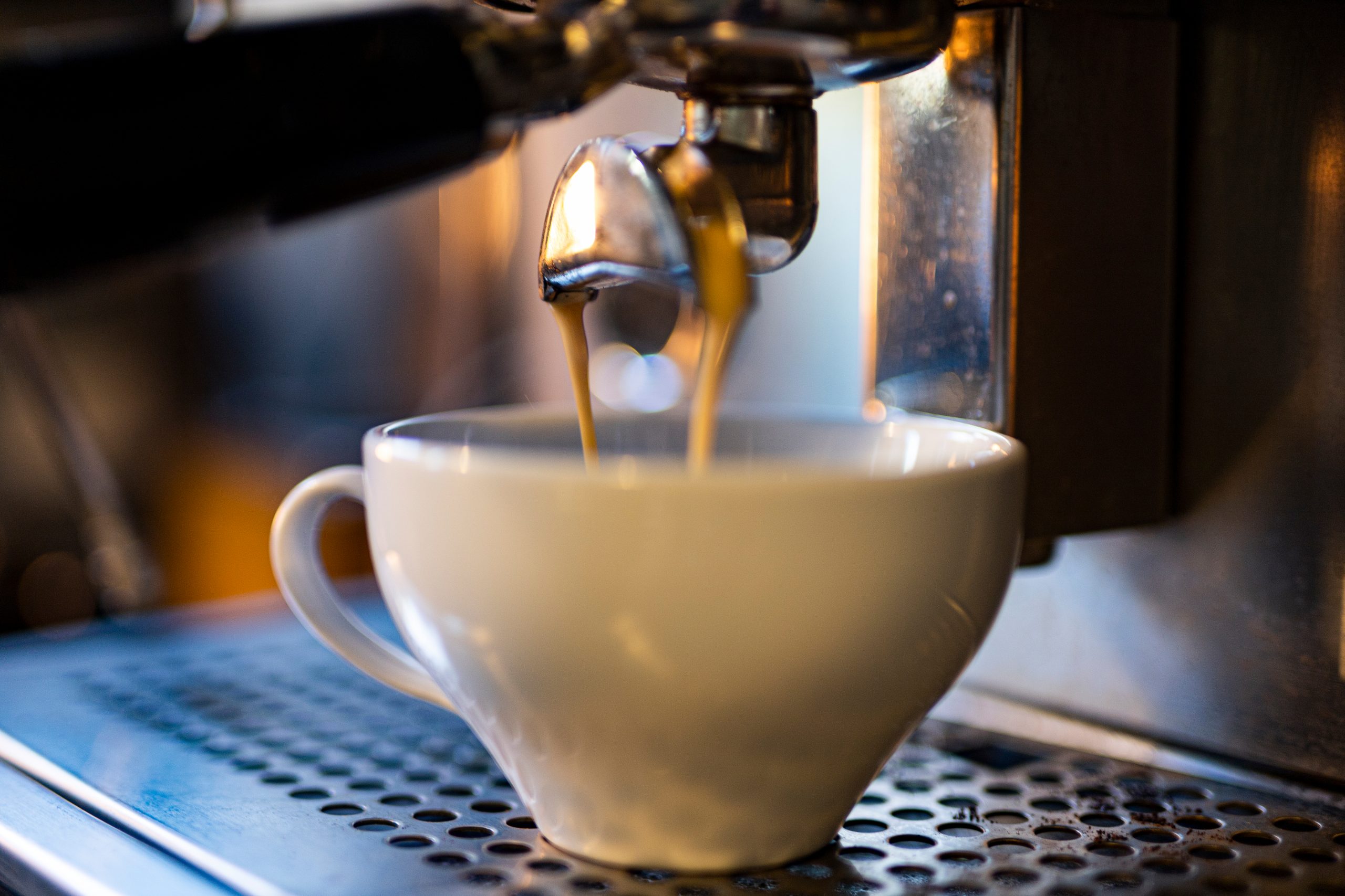 biała filiżanka, do filiżanki leje się kawa z ekspresu