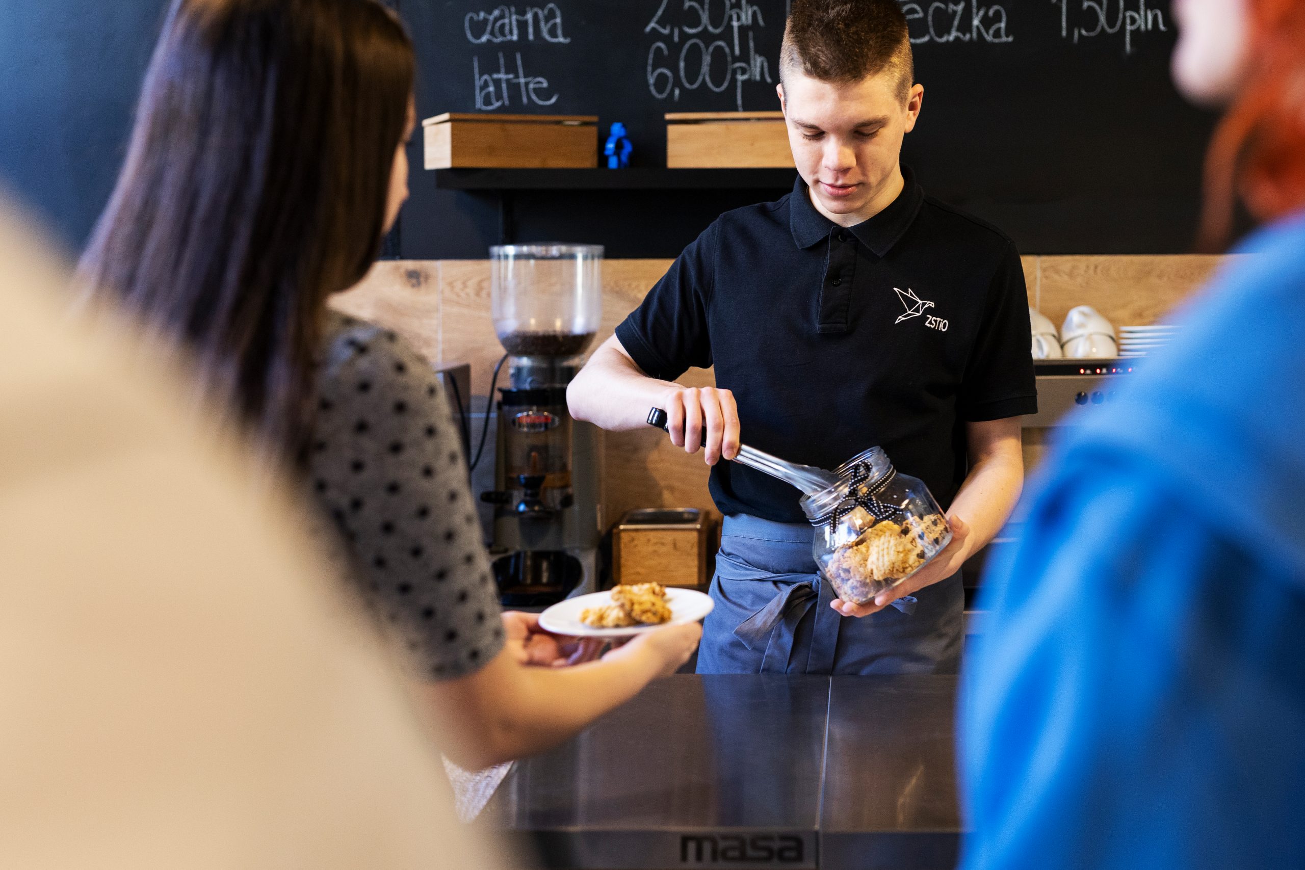 Młody chłopak-kelner wyjmuje szczypcami ciastka ze słoika