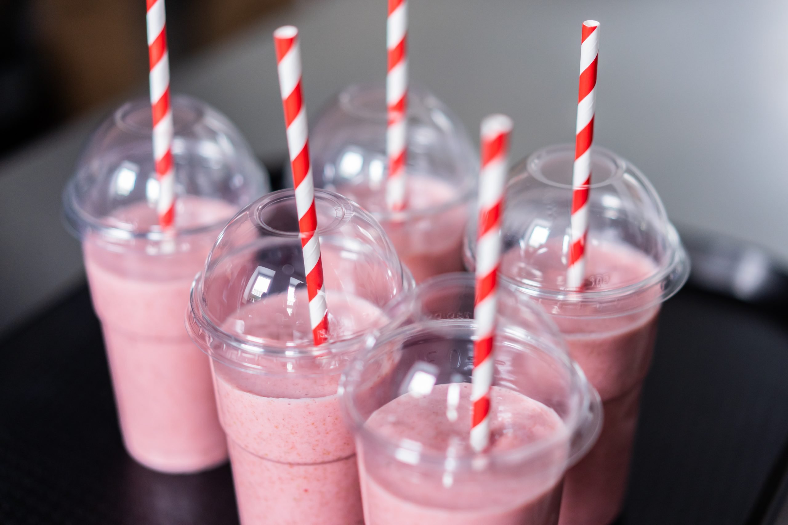 5 plastikowych kubków z różowym napojem i słomkami biało-czerwonymi