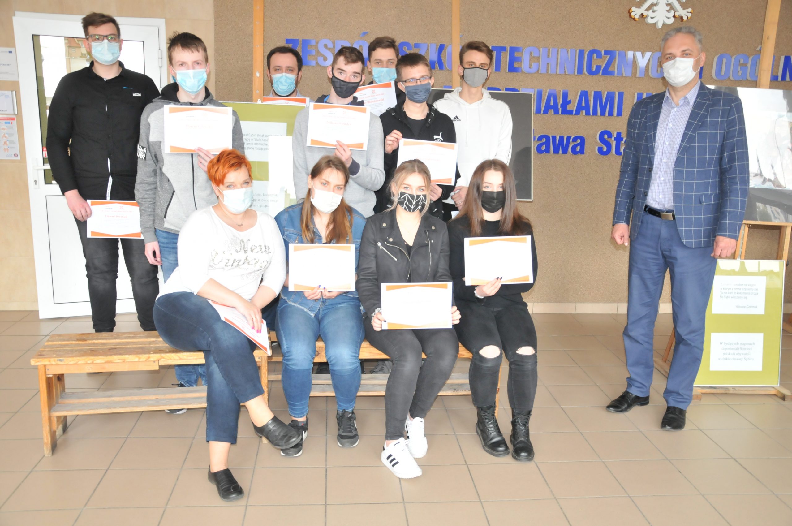 grupa uczniów i nauczycieli siedzi i stoi, trzyma w ręku certyfikaty
