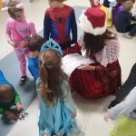 na podłodze siedzą dzieci, dziewczyna przebrana w strój historyczny rozdaje naklejki