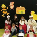 w tle zwierzęta, na pierwdszym planie siedzą dzieci, z tyłu cztery dziewczyny przebrane w historyczne stroje