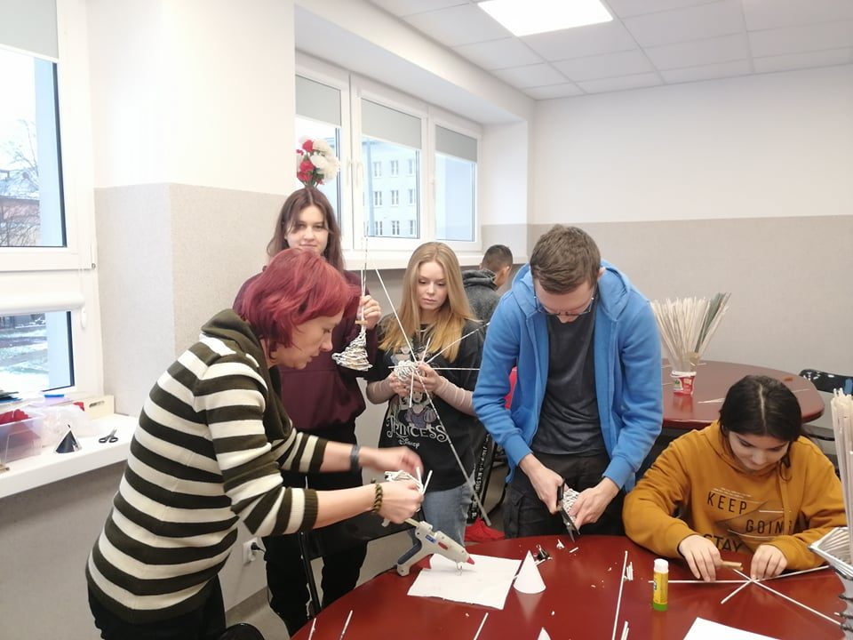 grupa ludzi trzyma w rękach rurki z papieru, tworzą dekoracje świąteczne