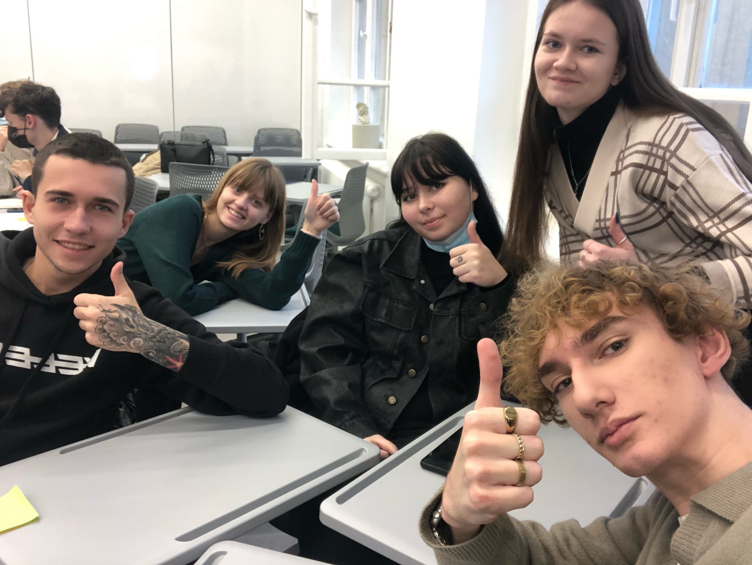 grupa młodych uczniów, siedzi przy stoliku, patrzy w obiektyw, unosi kciuki do góry