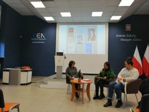 trzy kobiety siedzą na fotelach, jedna z mokrofonem, w tle prezentacja