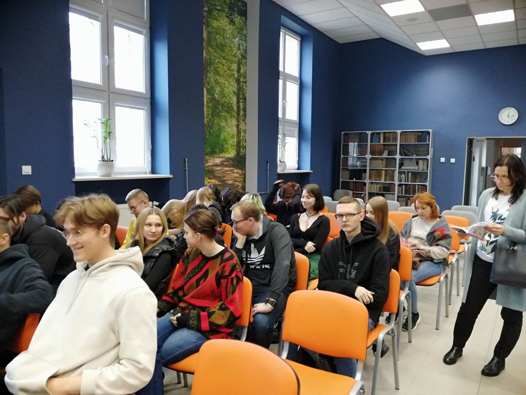 grupa uczniów siedzi na krzesłąch w sali konferencyjnej