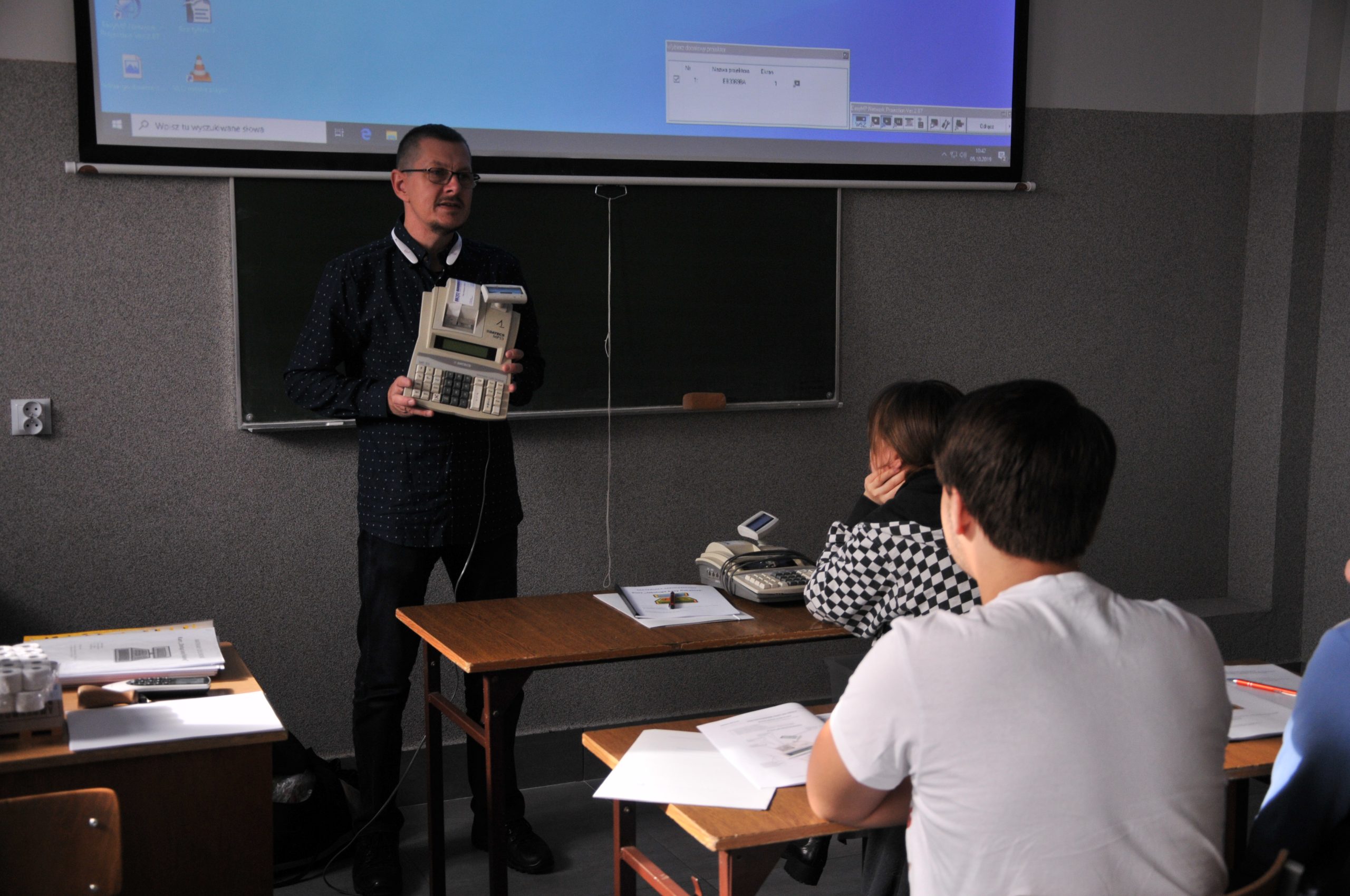 nauczyciel z urządzeniem elektronicznym na tle tablicy