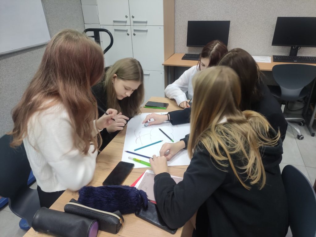 5 uczennic siedzi przy biurku, na stole piórniki, mazaki, kredki, kartki