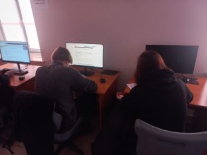 grupa uczniów siedzi przy stoiskach komputerowych w sali lekcyjnej