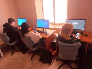 grupa uczniów siedzi przy stoiskach komputerowych w sali lekcyjnej