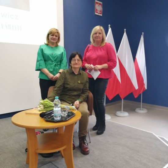 trzy kobiety, dwie stoją, jedna siedzi, w tle polskie flagi