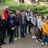 grupa uczniów i nauczycieli stoi na podwórku na placu szkoły