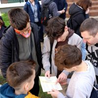 grupa uczniów pochyla się nad kartką, czytają