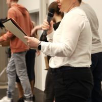 kobieta stoi na scenie z mikrofonem, czyta z kartki