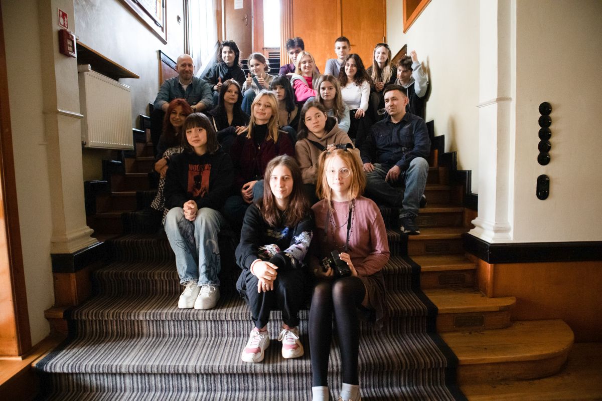 grupa uczniów siedzi na schodach szkoły filmowej