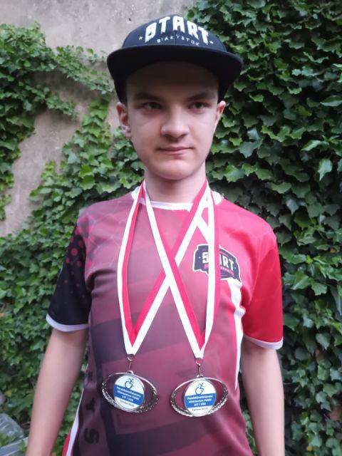 chłopak w sportowej czapce, w cvczerwonej koszulce i z dwoma medalami