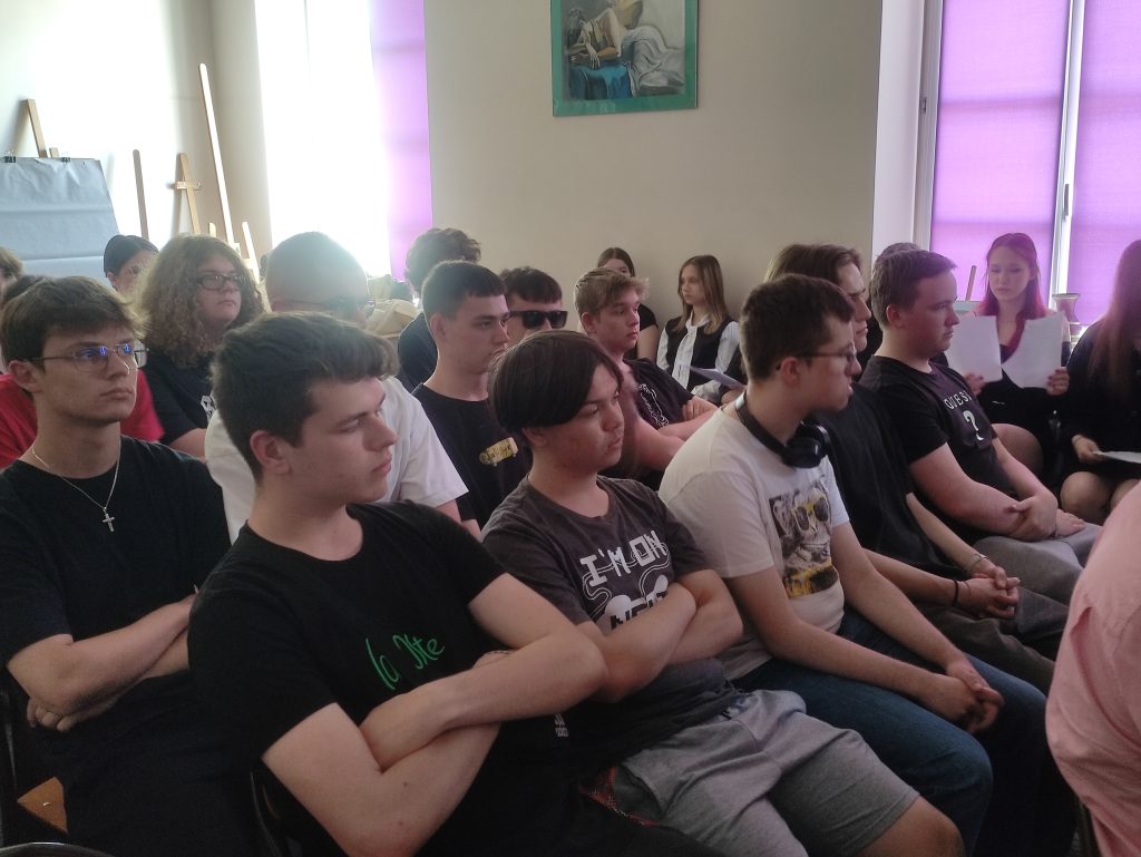 grupa uczniów siedzi na krzesłach w sali szkolnej